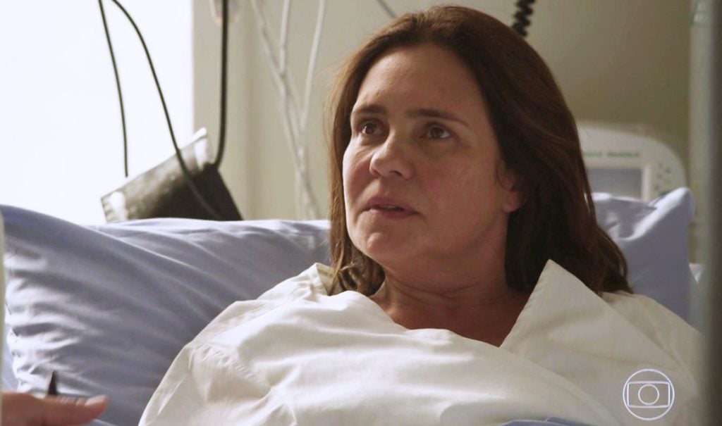 Atriz Adriana Esteves deitada na cama de um hospital em cena da novela Amor de Mãe da Globo