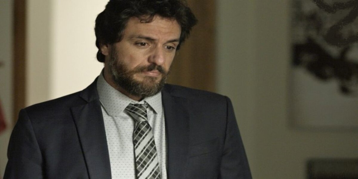 Rodrigo Lombardi em cena da novela A Força do Querer, ele usa terno cinza escuro, camisa social clara e gravada quadriculada, barba e tem expressão de dúvida