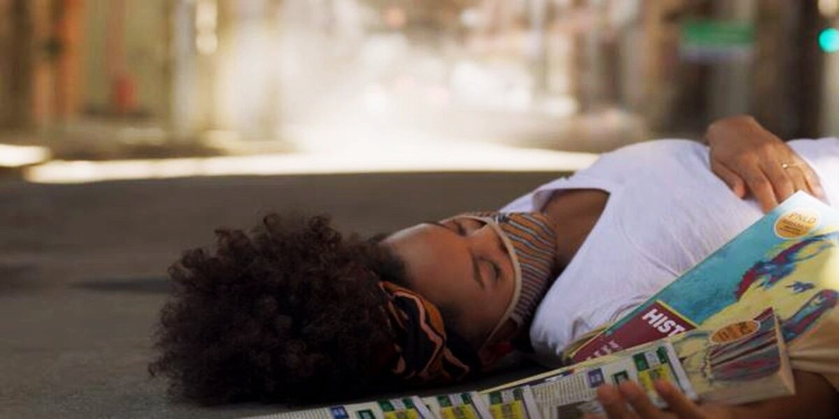 Camila, mulher negra de cabelo black power, caída na rua com livros de história espalhados