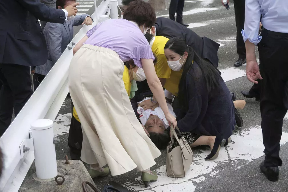 Abe com camisa ensanguentada e mãos no peito caído no chão (Foto: Kyodo / via REUTERS) 