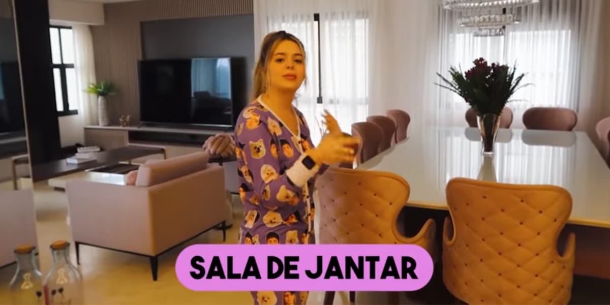 Sala de jantar em conceito aberto e com vista para a sala de estar, com uma grande televisão e sofá confortável (Reprodução: Youtube)