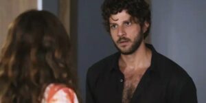 Ari veste camisa preta social aberta, barba e cabelos castanhos em cena da novela Travessia