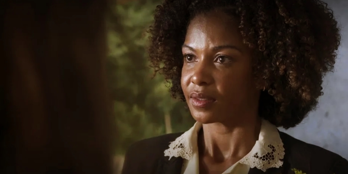 Dagmar é uma mulher negra, com cabelo blackpower médio que usa blazer preto e camisa branca em cena da novela Mar do Sertão