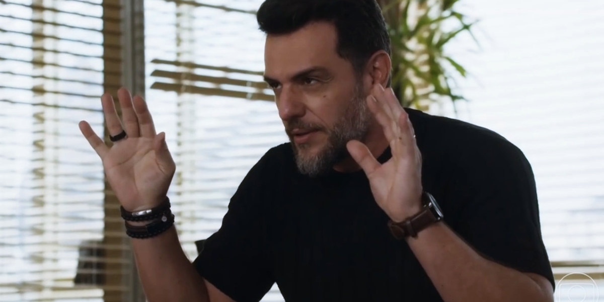 Moretti na novela Travessia usando camisa de manga curta azul, relógio marro e pulseiras pretas 