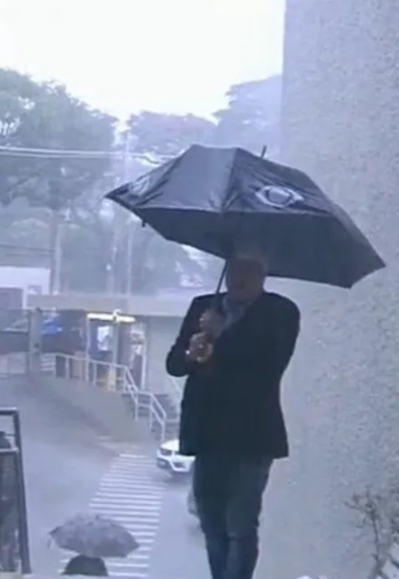 Datena fora dos estúdios mostrando a chuva antes do guarda-chuva quebrar (Foto: Reprodução/ Band)