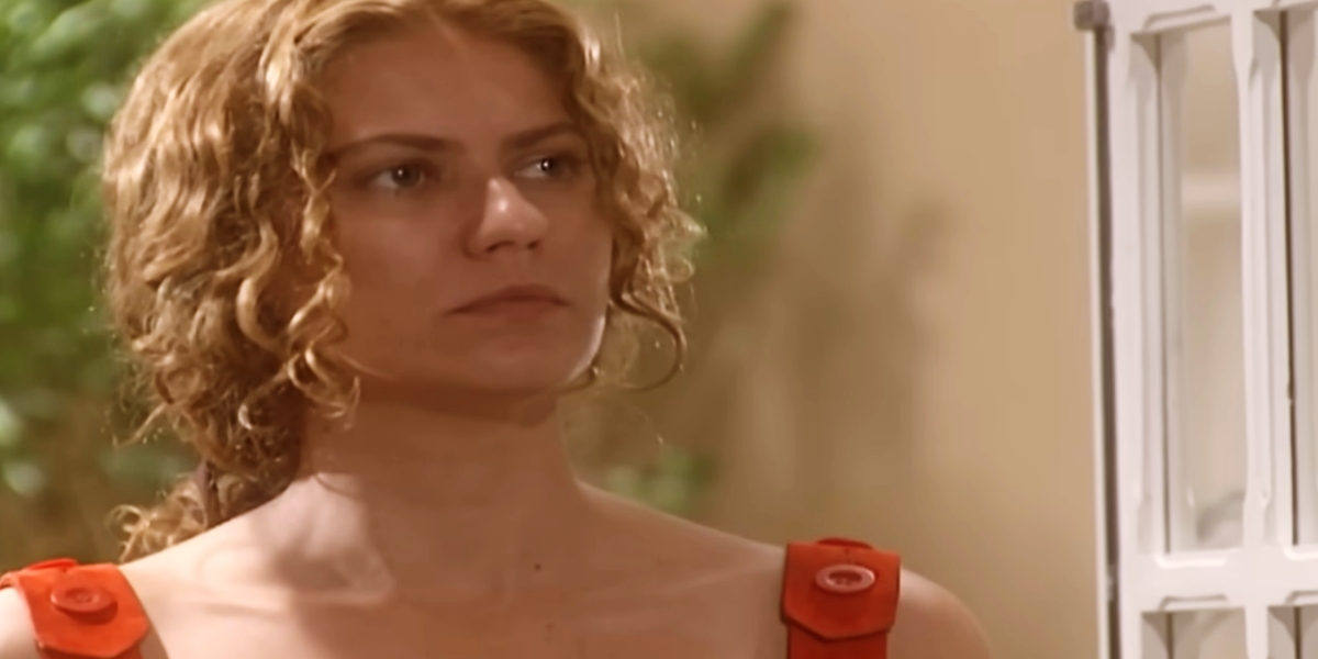 Luana com cabelo loiro preso, vestido de alça laranja em cena da novela O Rei do Gado