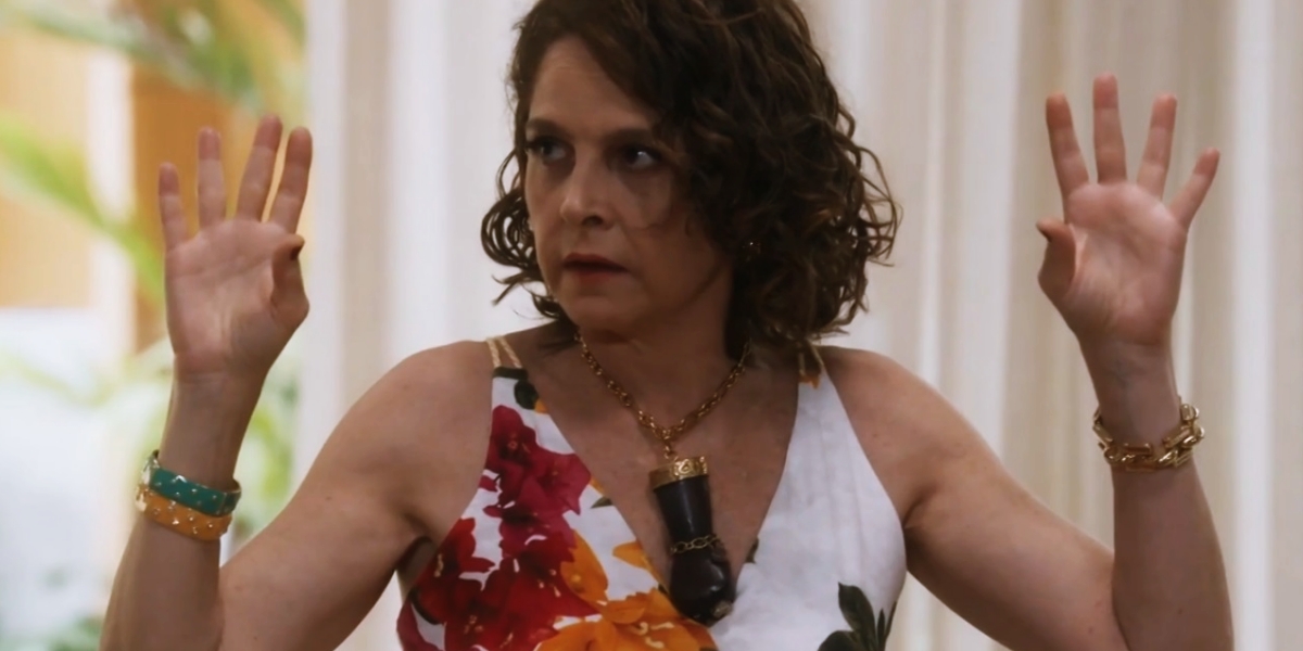 Núbia em cena da novela Travessia usando vestido florido e colar com grande mão preta com punho fechado