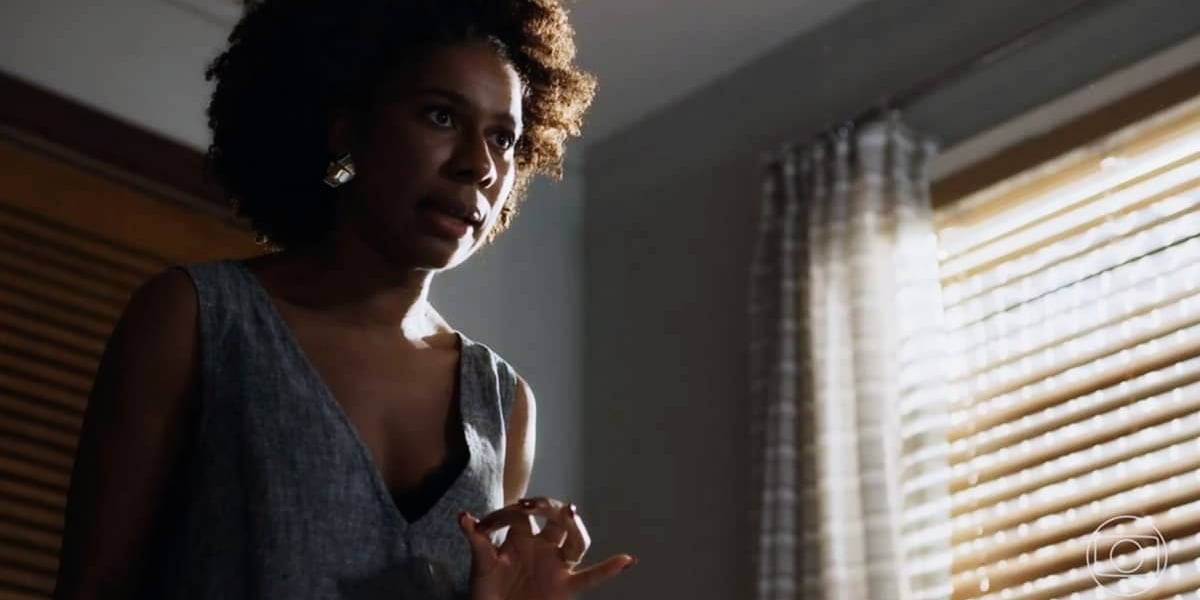 Laís (Indira Nascimento) mulher negra que usa vestido cinza está em cena da novela Travessia.