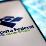 Celular sobre notas de cem reais, e com o aplicativo da receita federal aberto, no imposto de renda - Foto Reprodução Internet