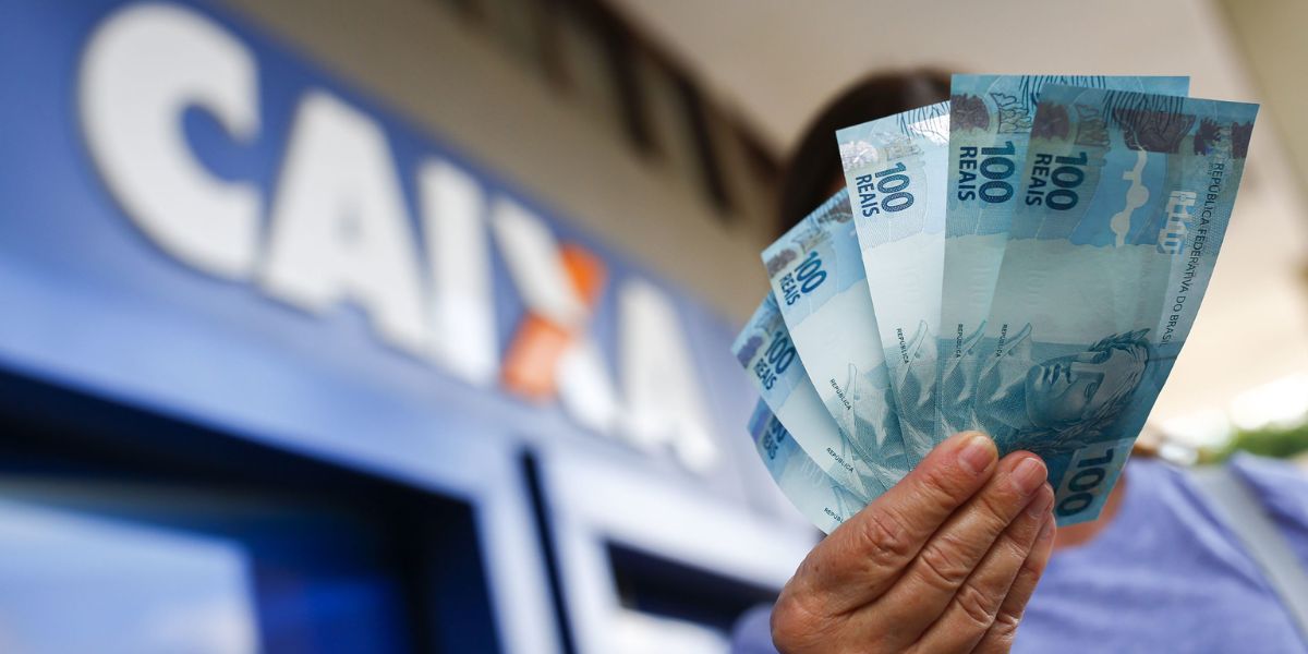 Person holding banknotes in front of a Caixa branch - Internet photo reproduction