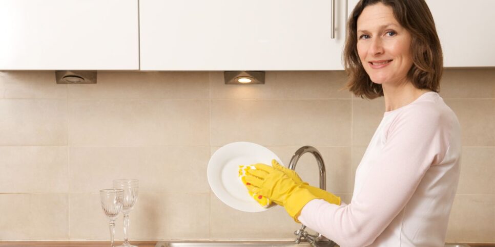 Mulher lavando louça com luvas (Foto: Reprodução / Canva)